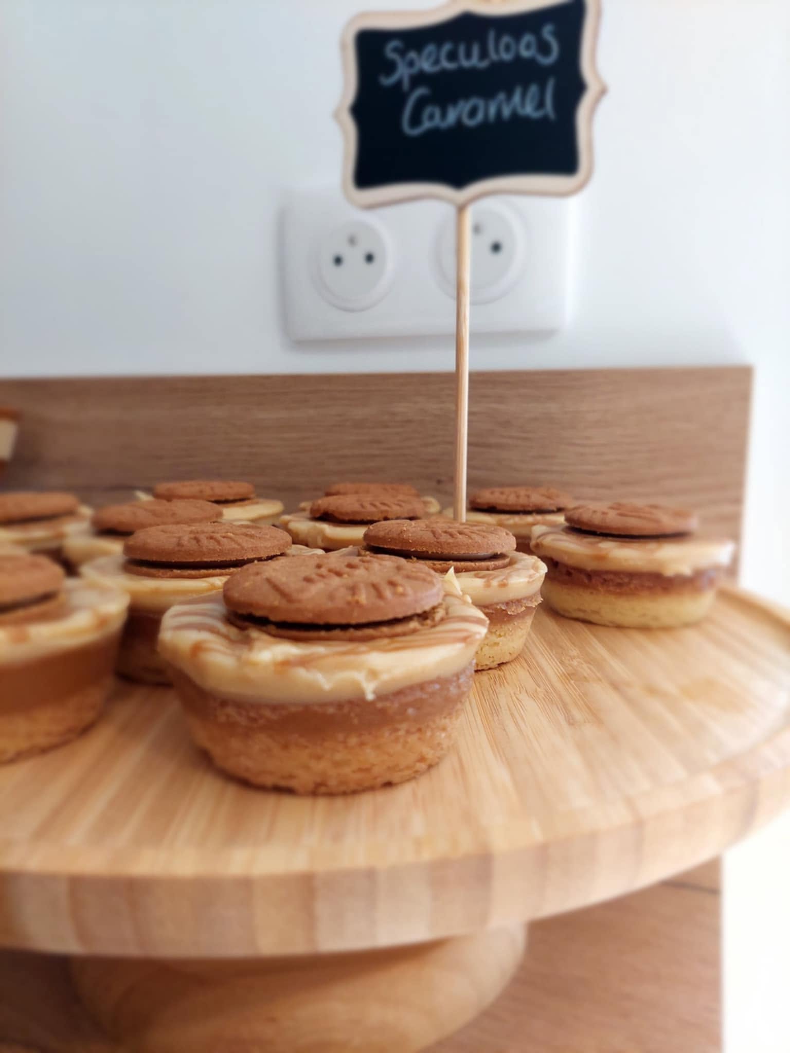 Individual speculoos caramel cheesecakes topped with caramel swirls and biscuits on a wooden cake stand with a chalkboard label