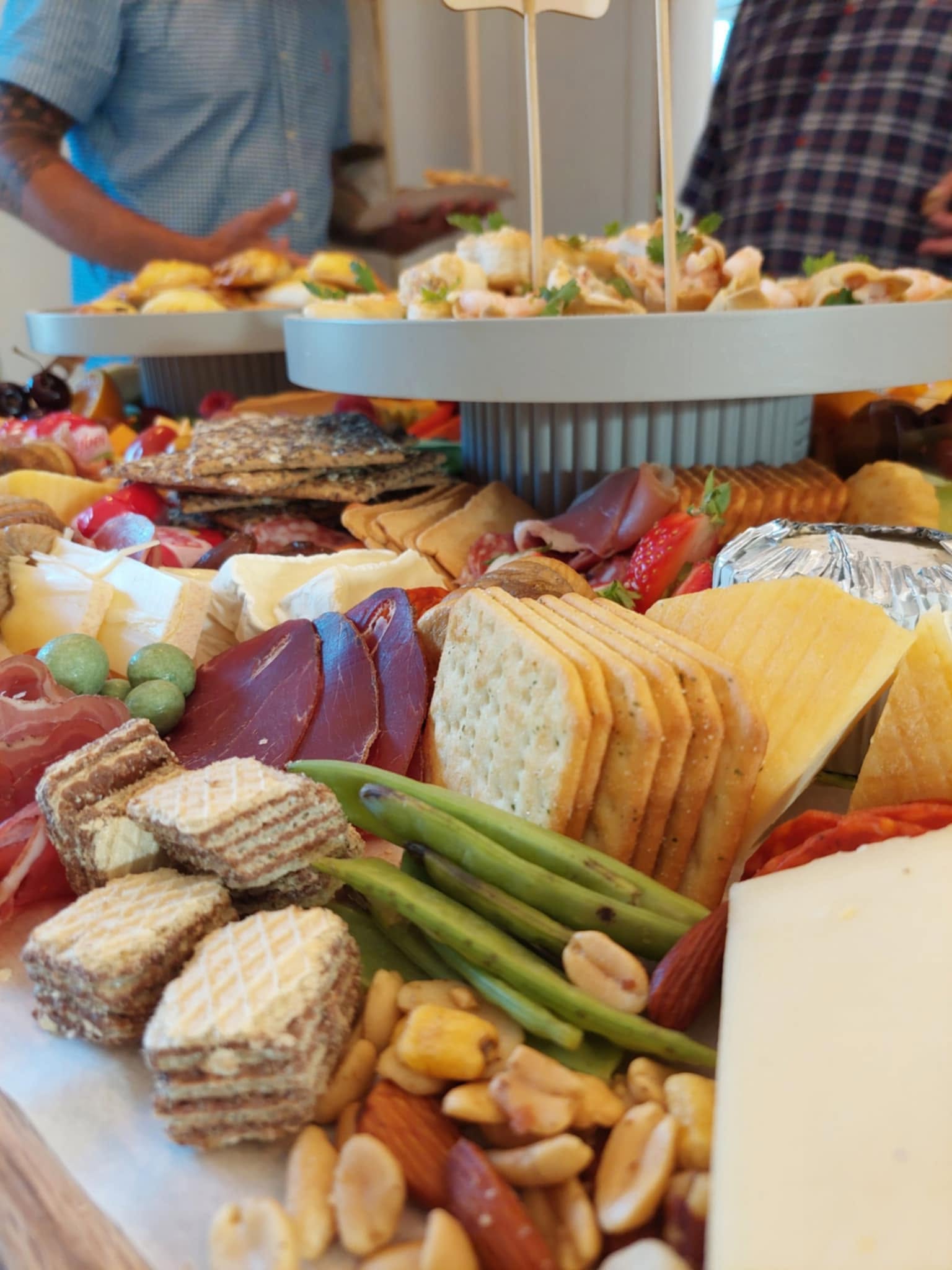 Guests helping themselves to tiered platters of prawn vol-au-vents above boards of cheese, cured meats and wafers