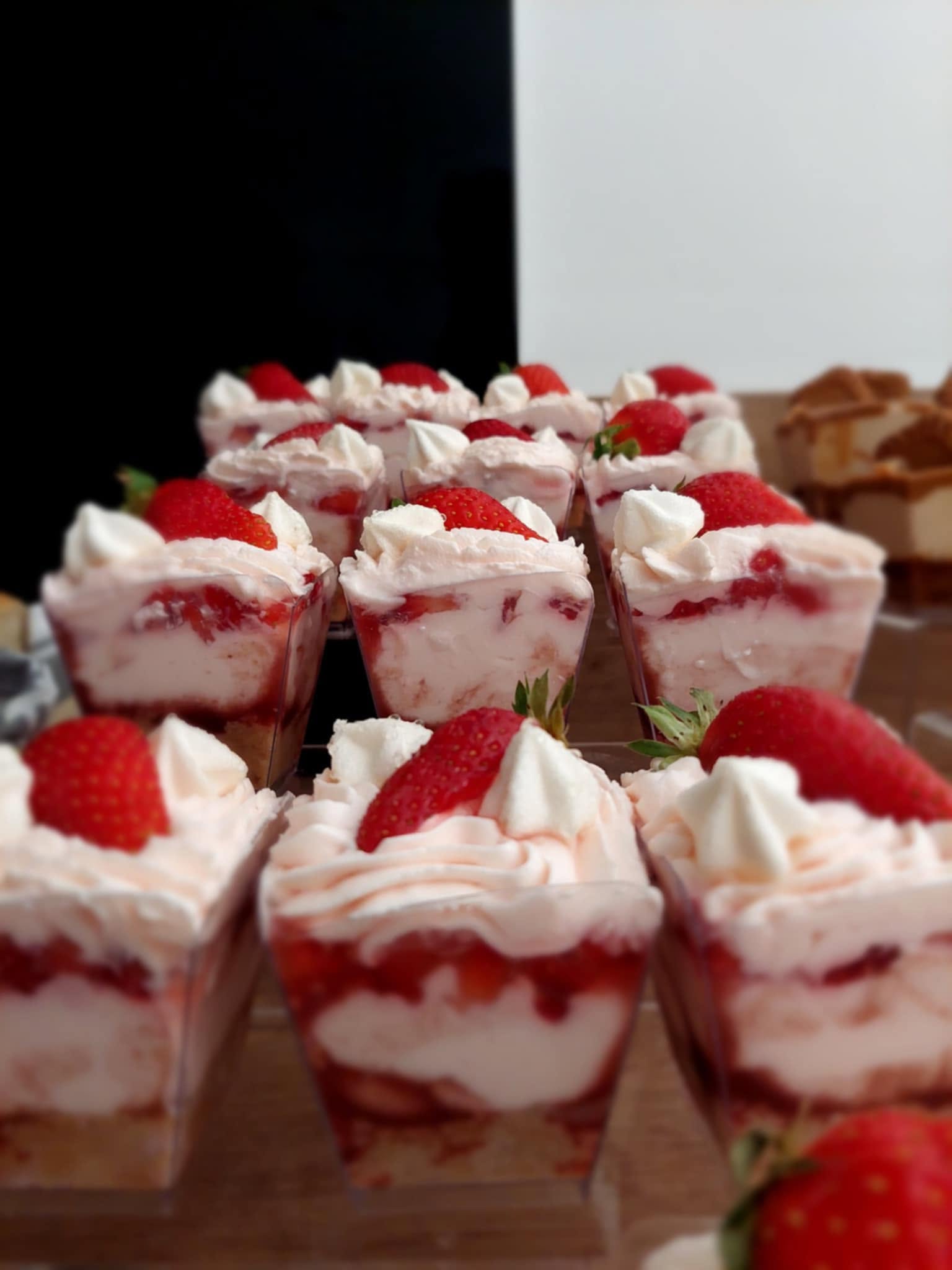 Rows of individual strawberry dessert cups layered with sponge, cream and fresh strawberries, finished with a meringue kiss