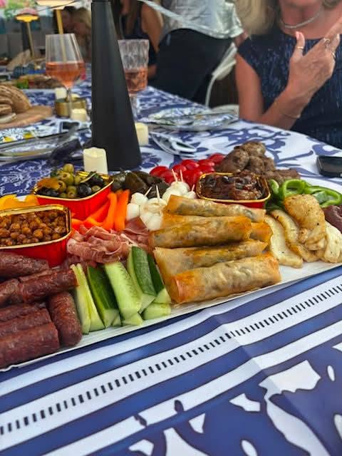 The same mezze platter served on a blue patterned table outdoors with guests seated around it