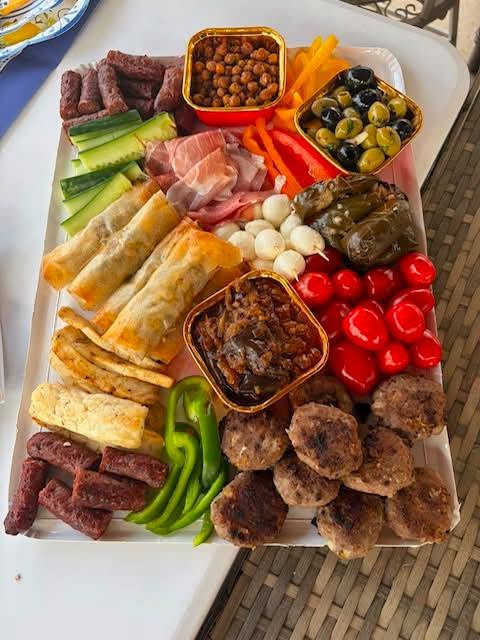 An overhead mezze platter of kofte meatballs, cured sausage, prosciutto, crispy borek cigars, fried halloumi, dolmades, stuffed peppers, olives, roasted chickpeas and cucumber batons